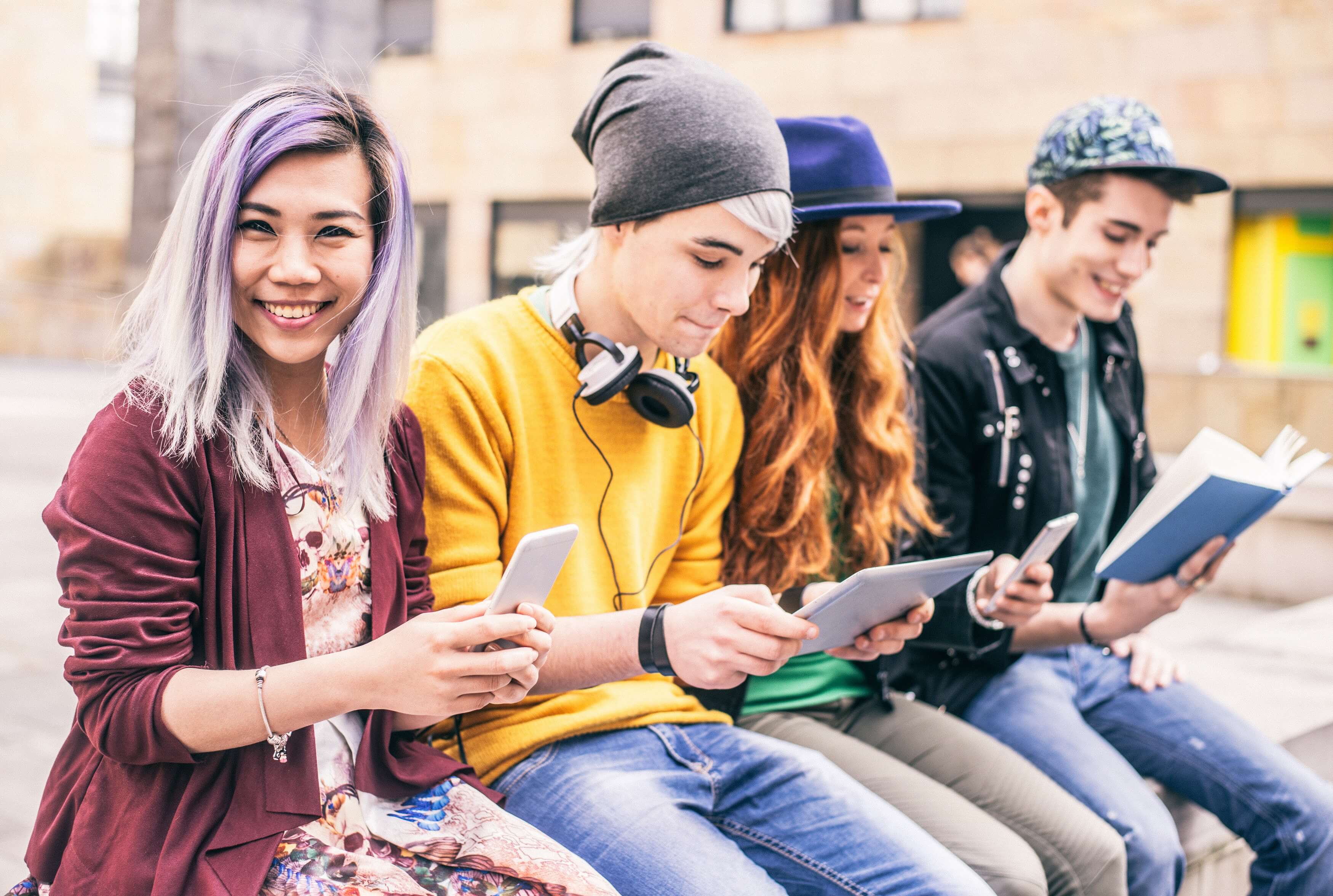 Four young people reading books and devices sit together outside